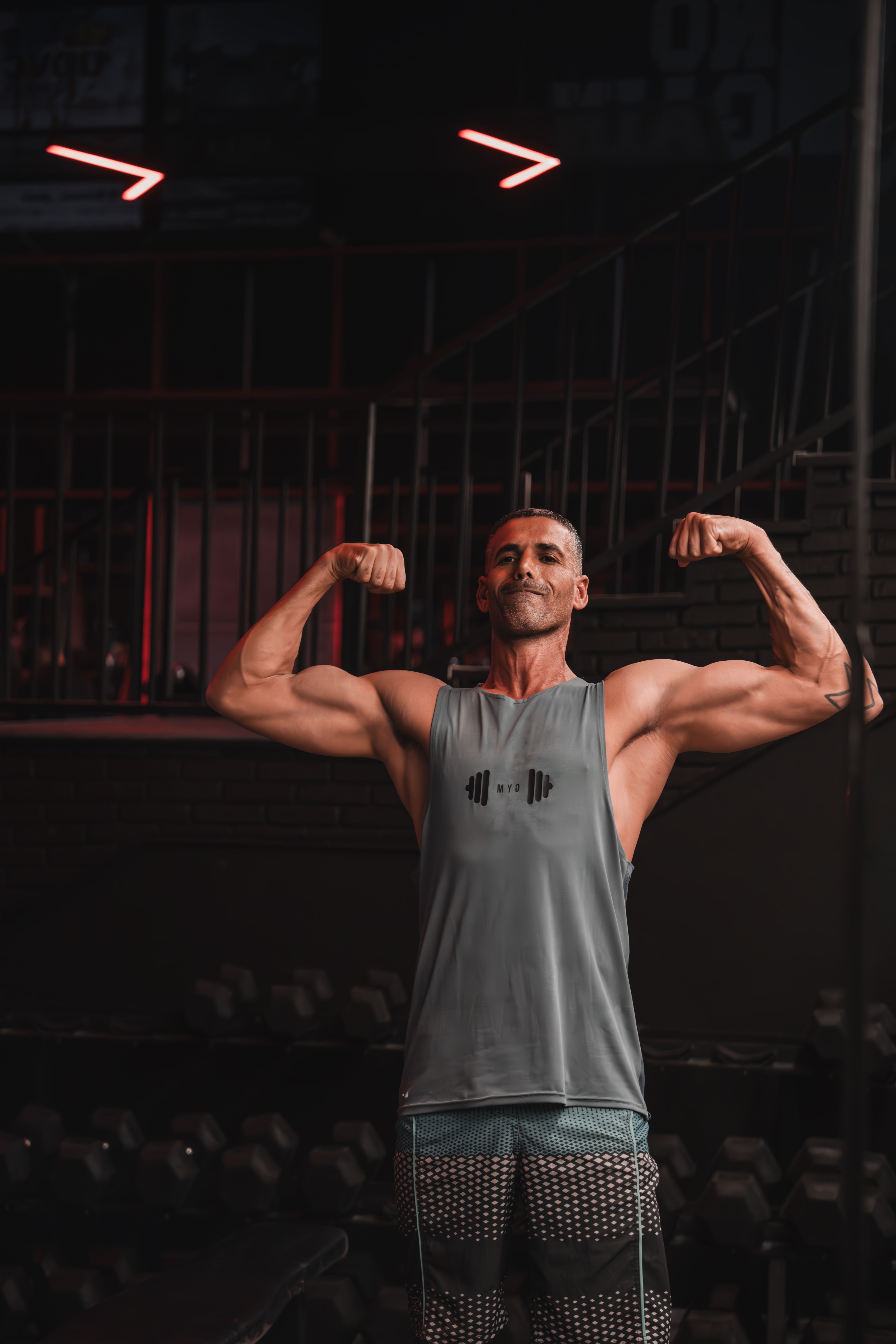 Athletic man posing and flexing muscles in a dimly lit gym.