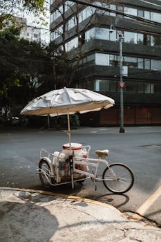 Pedal cart with umbrella on quiet urban street corner, showcasing urban life.
