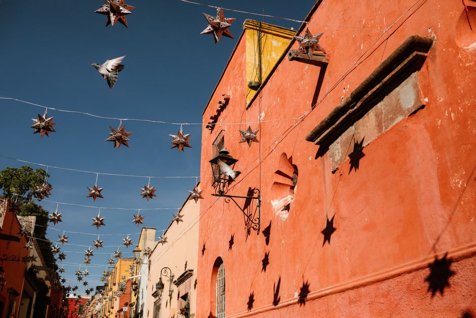 Vibrant street scene in San Miguel de Allende with decorative star lights and vivid orange walls at golden hour