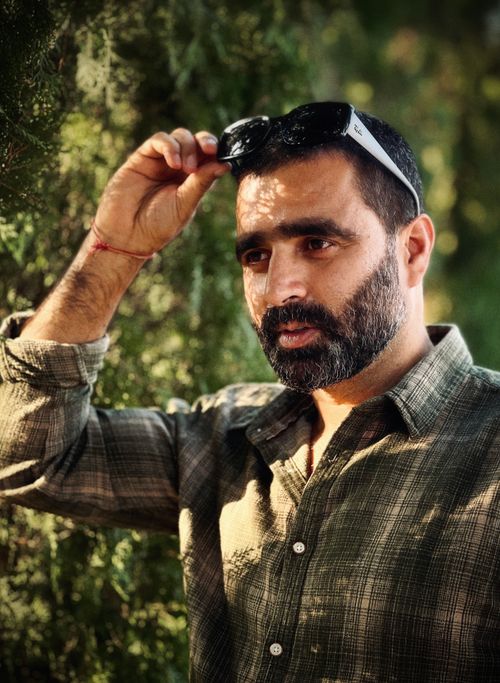 Free Bearded man adjusts sunglasses in sunlight, surrounded by lush greenery. Stock Photo