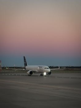 A commercial airplane on the tarmac at dusk under a pastel sky with runway lights.
