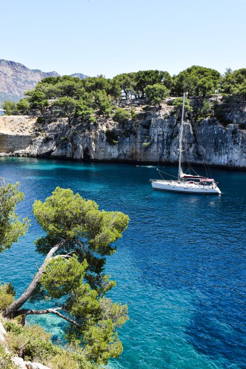 Free Stunning sailboat sailing in crystal clear waters of Calanques, France, surrounded by lush green cliffs. Stock Photo