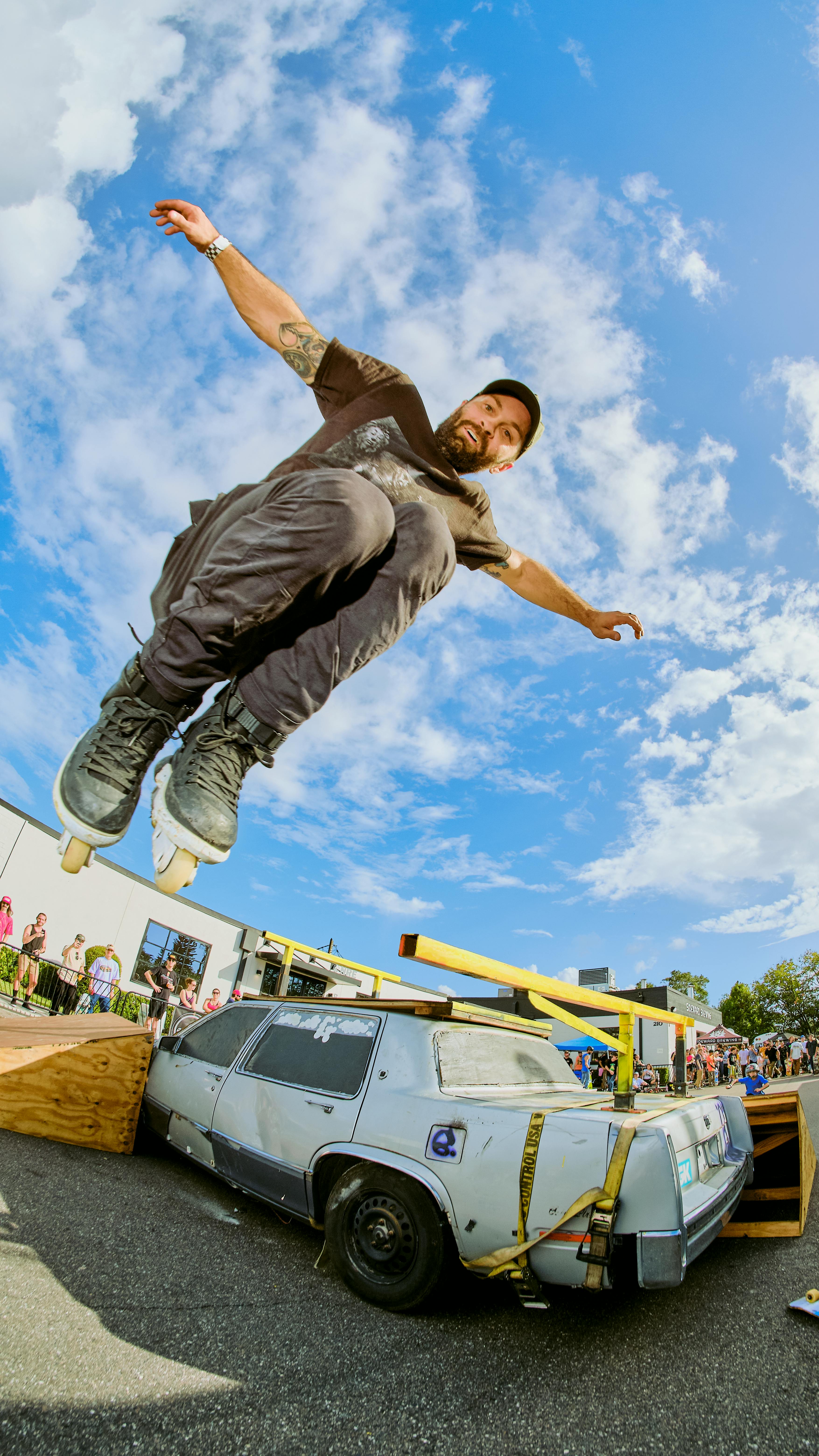 Skater performing an acrobatic jump over a vintage car during an outdoor event. Energetic and thrilling.