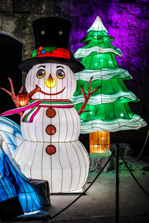 Free Brightly lit snowman and Christmas tree with colorful lights, creating a joyful winter scene. Stock Photo
