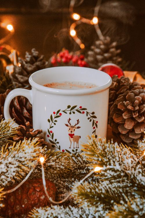 Free Warm festive atmosphere with hot chocolate in a reindeer mug surrounded by pinecones and lights. Stock Photo