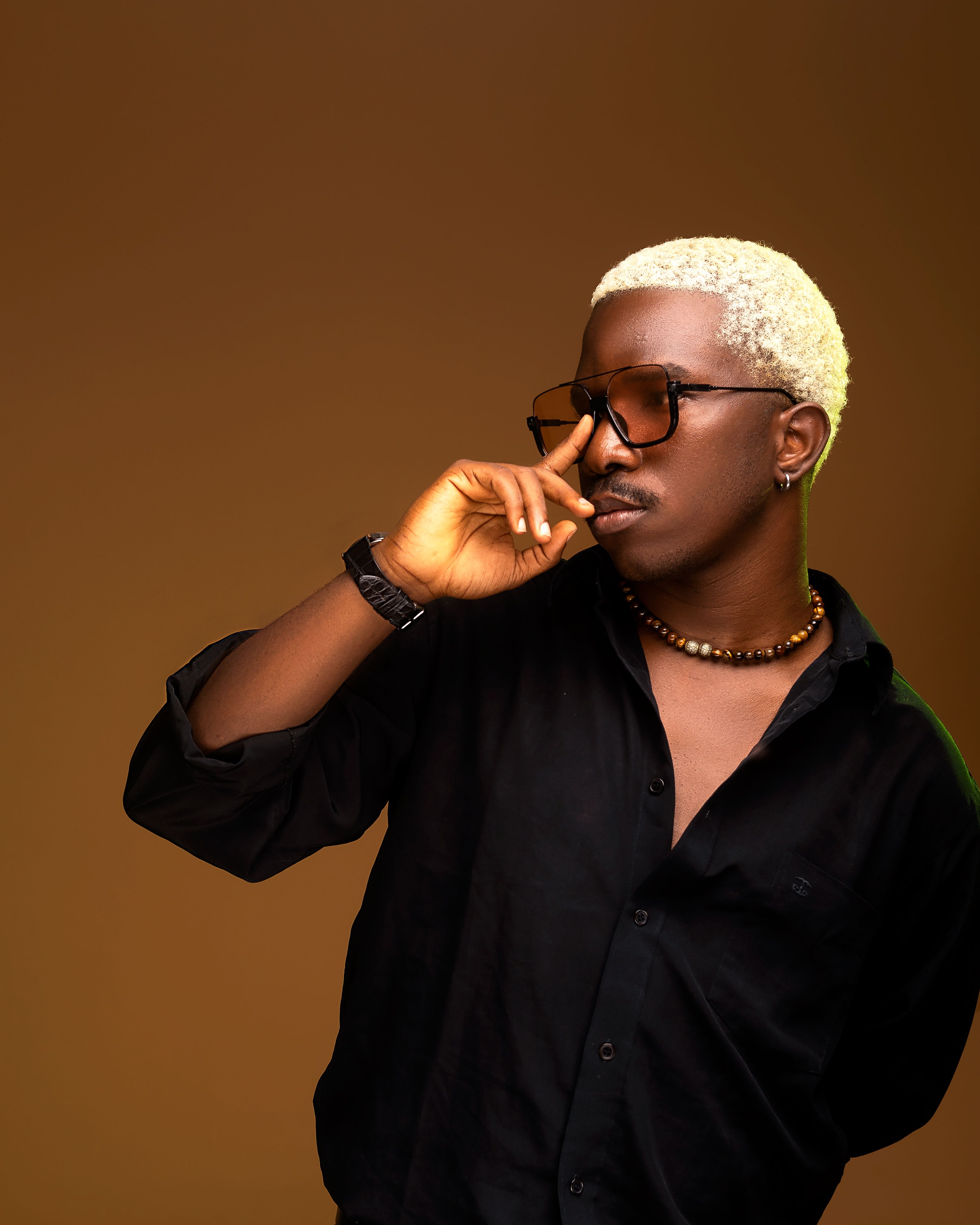 Fashionable man in black shirt with blonde hair wearing sunglasses against a brown background.