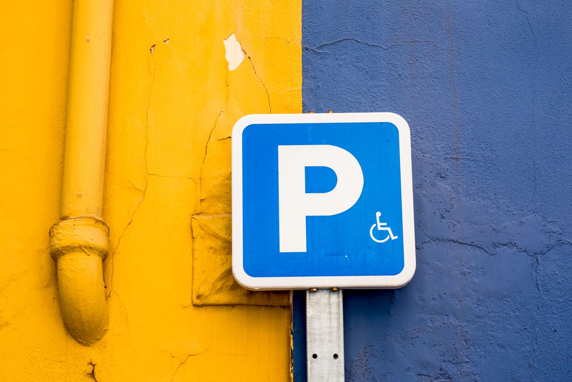 A blue parking sign against vibrant yellow and blue walls, symbolizing accessibility.