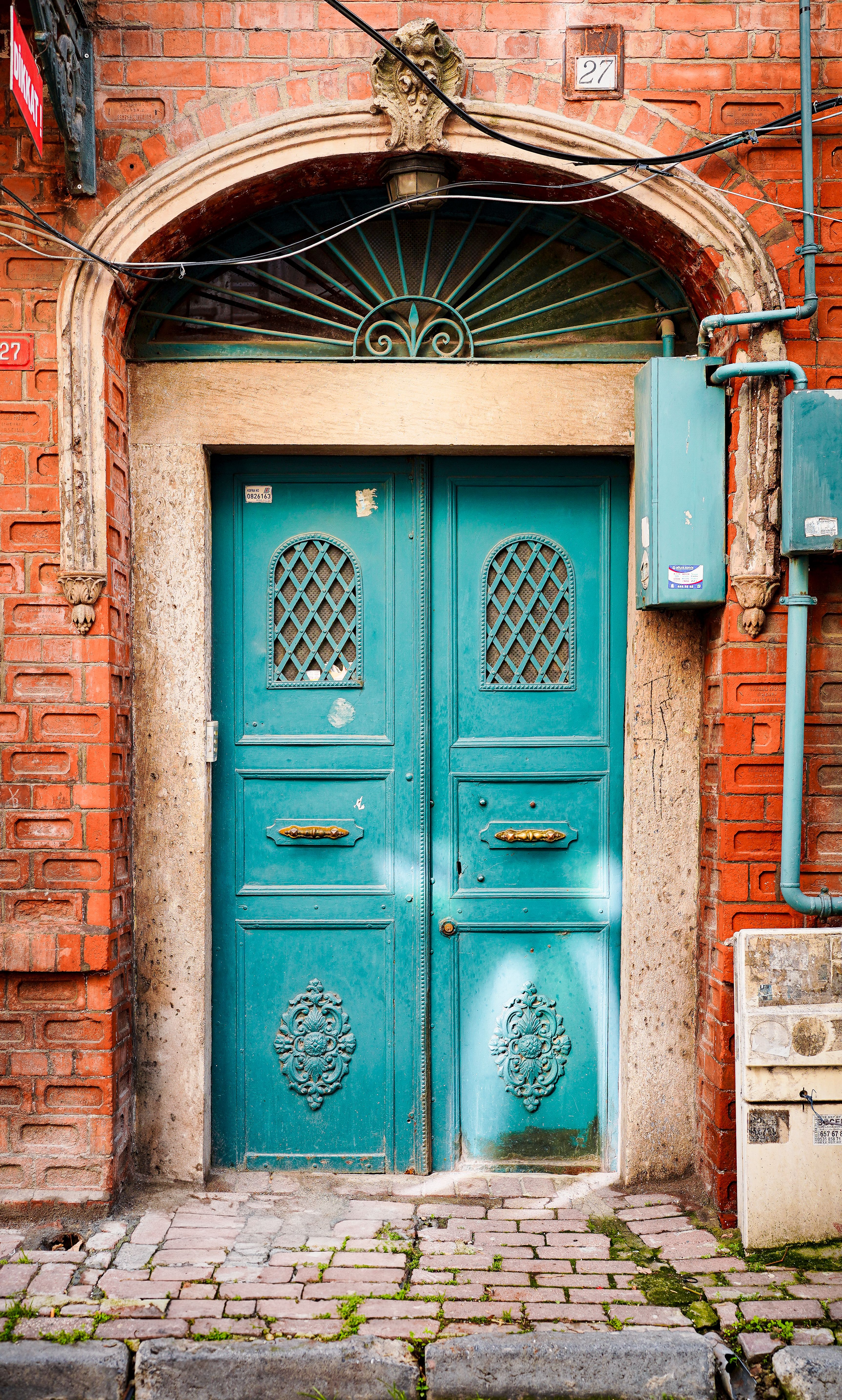 Old teal door with intricate design set in a rustic brick building facade.