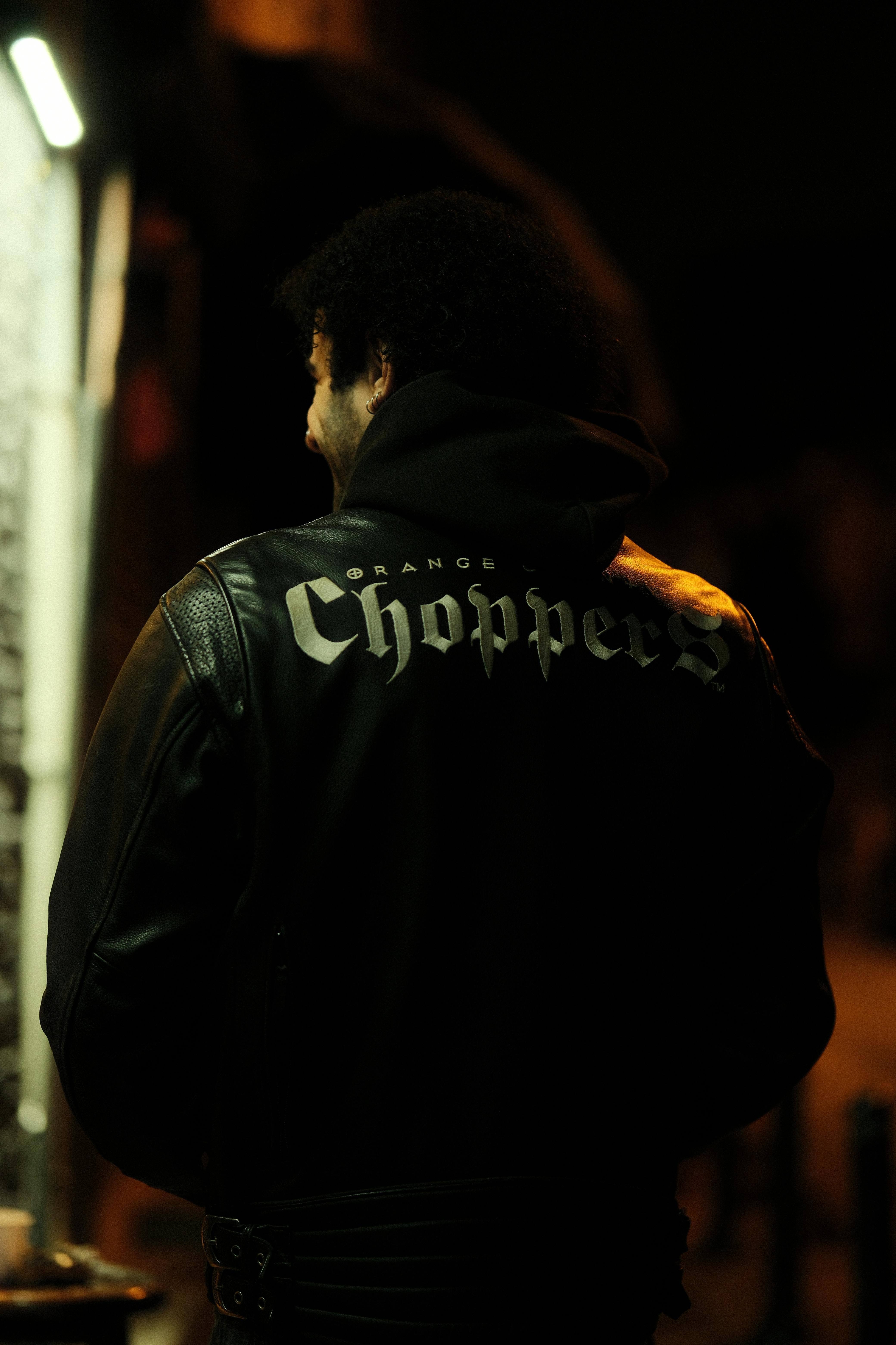 A person wearing a leather jacket with 'Choppers' text, photographed at night.