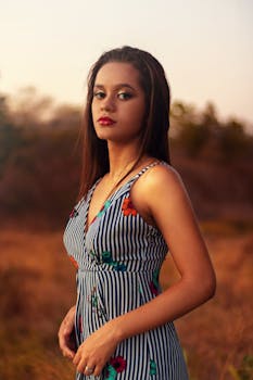 日落时分，一位身着条纹连衣裙的女子在户外摆出宁静的肖像姿势
