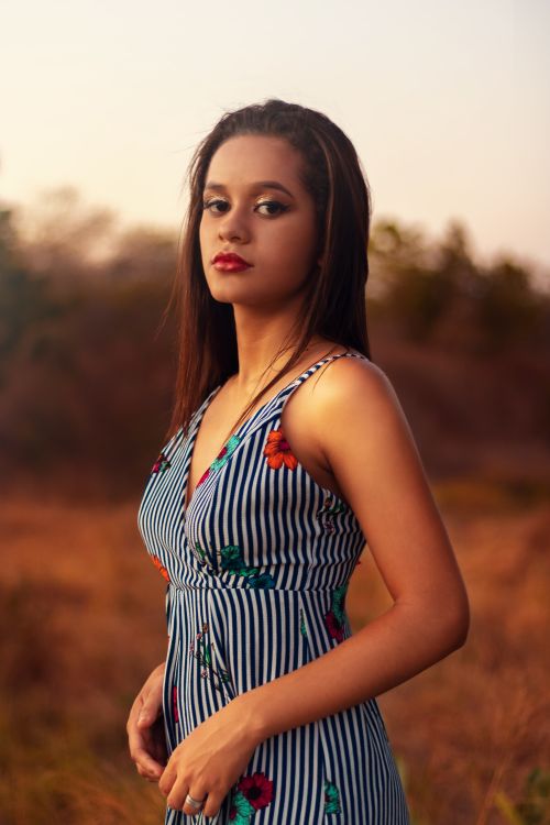 Free A serene portrait of a woman in a striped dress posing outdoors during sunset. Stock Photo