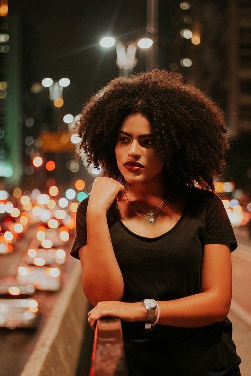 Free A fashionable woman with curly hair poses on a city street at night. Stock Photo