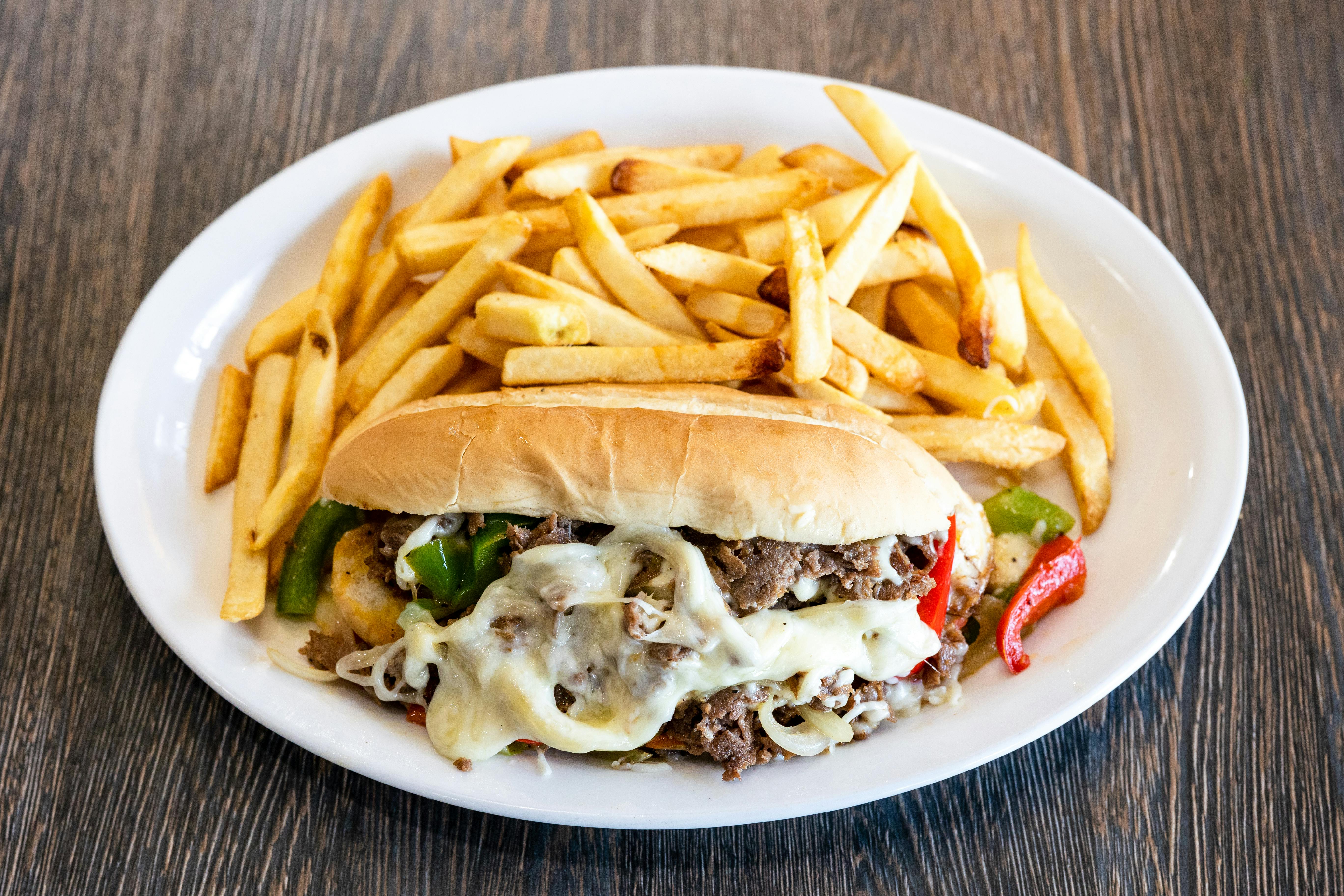 Free Mouth-watering Philly cheesesteak with melted cheese and french fries. Stock Photo
