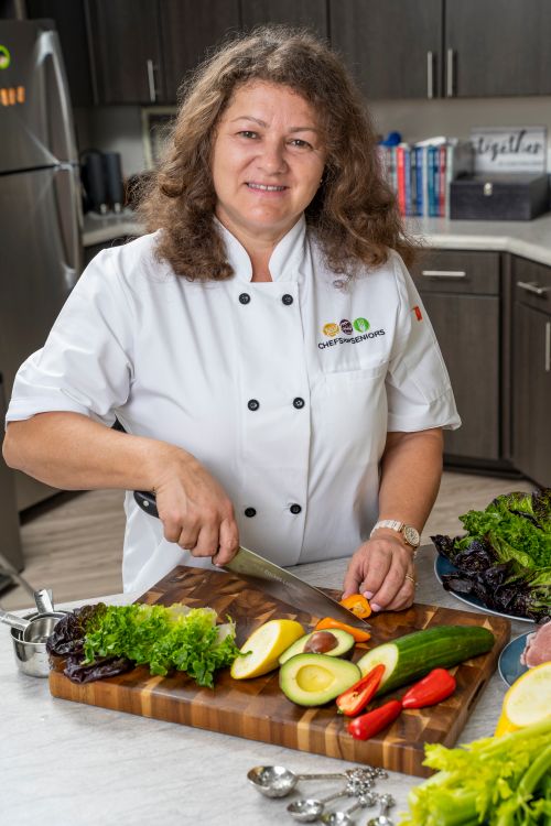 Free Chef slicing fresh vegetables in a modern kitchen setup featuring a variety of colorful produce. Stock Photo