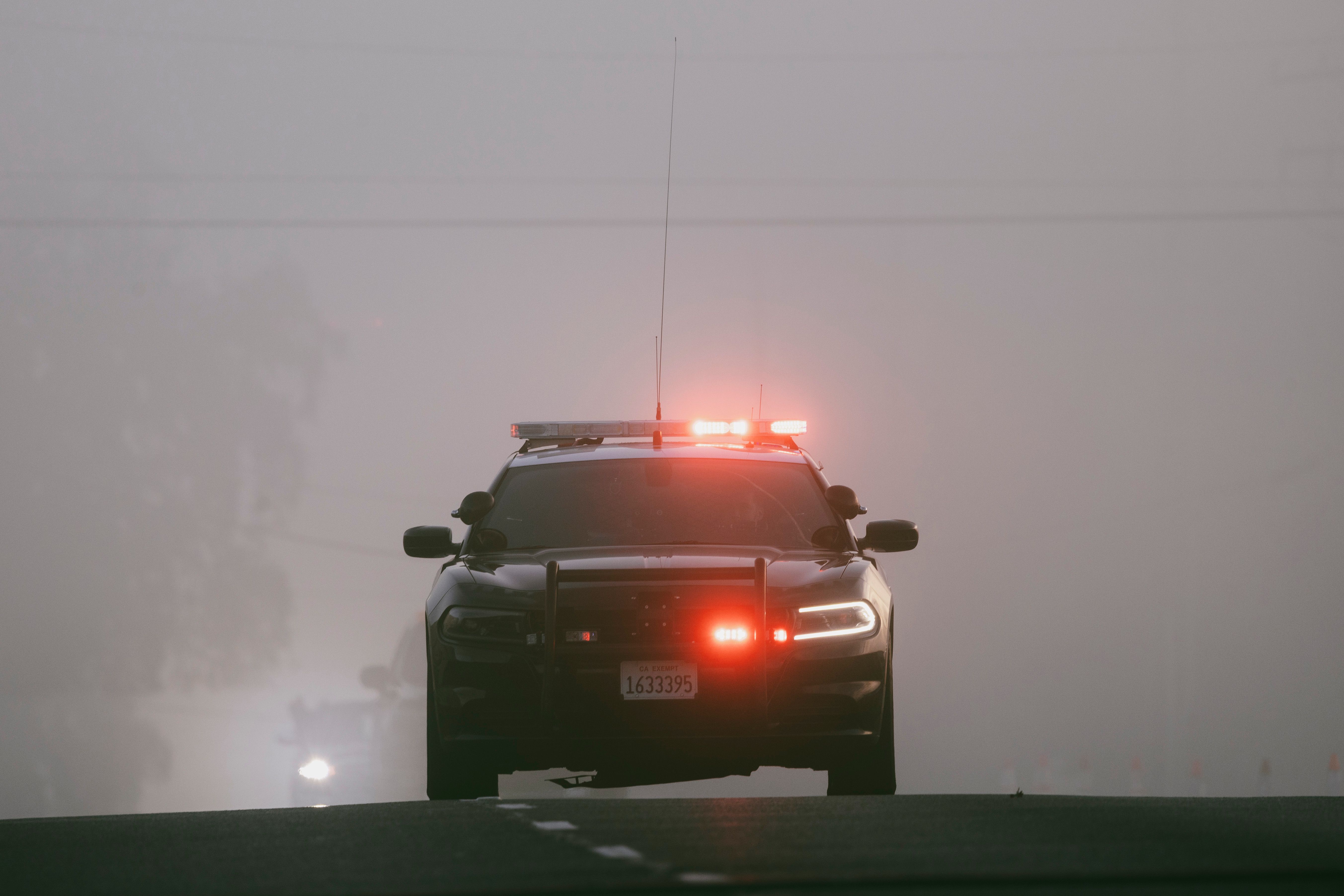 Gratis Le luci rosse illuminano una strada nebbiosa mentre si avvicina un'auto della polizia, creando un'atmosfera intensa. Foto a disposizione