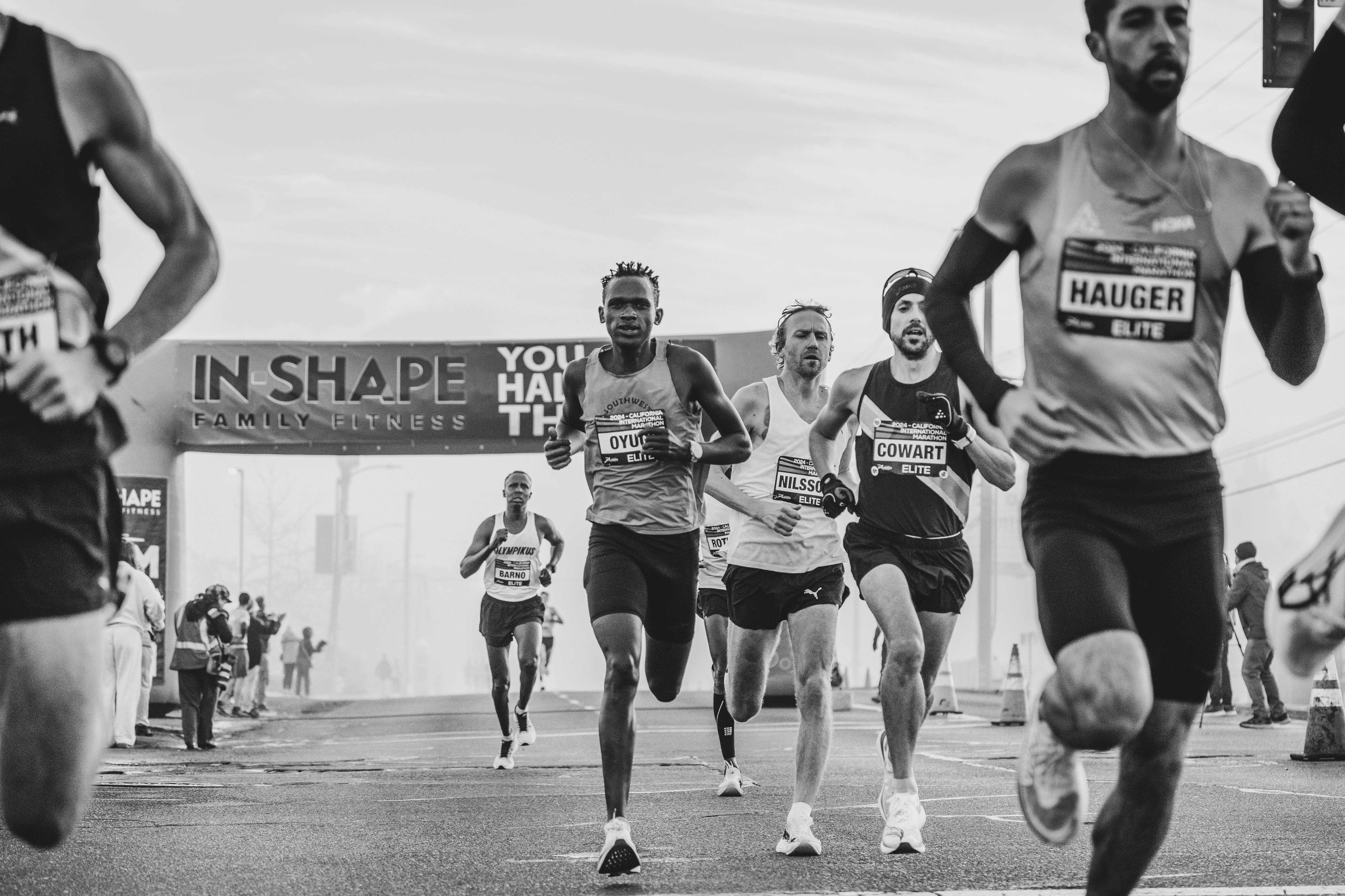 Black and white photo of intense marathon runners nearing the finish line under a large banner.