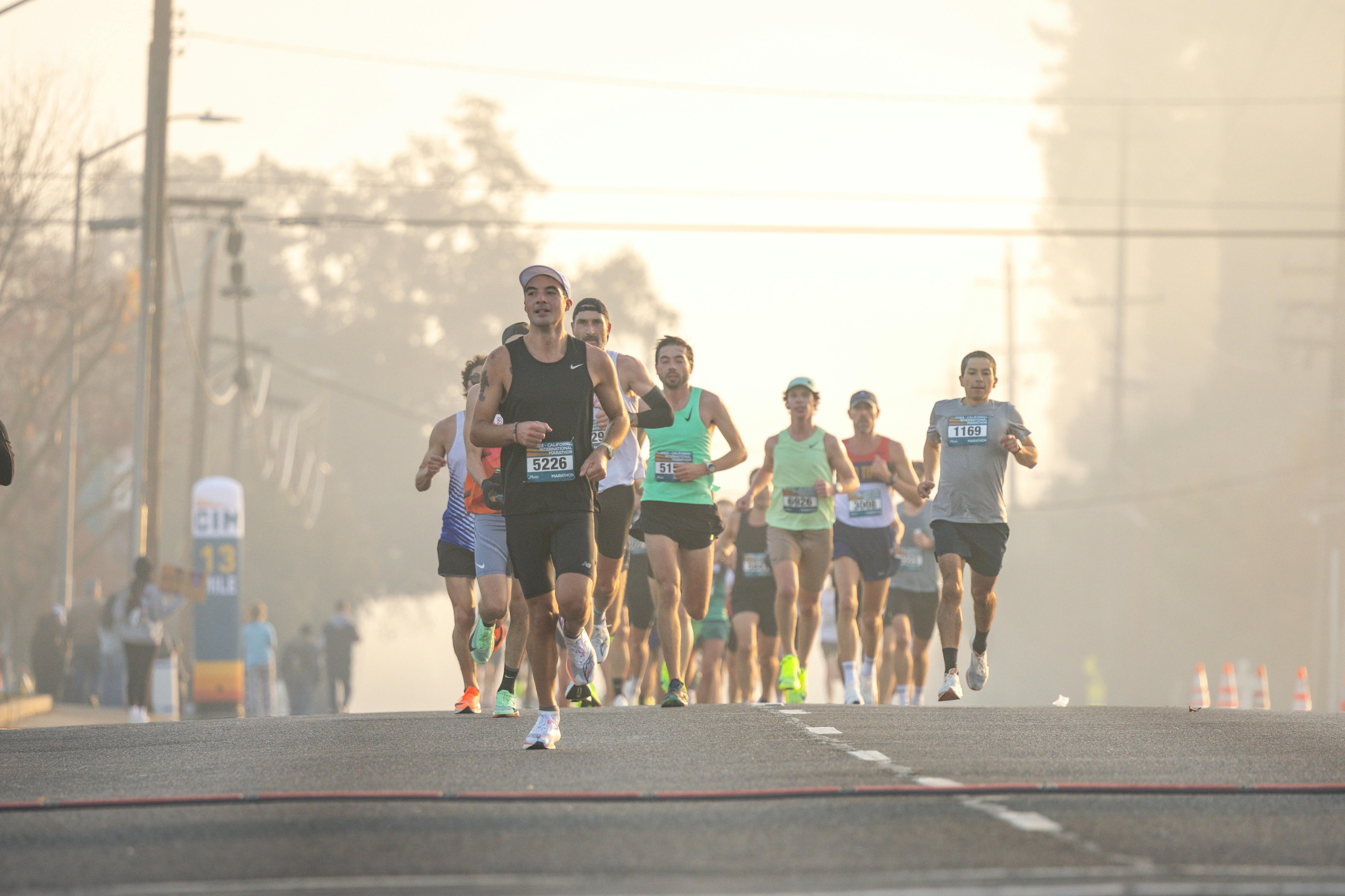 Group of runners in a marathon race on a foggy morning street with trees in the background.