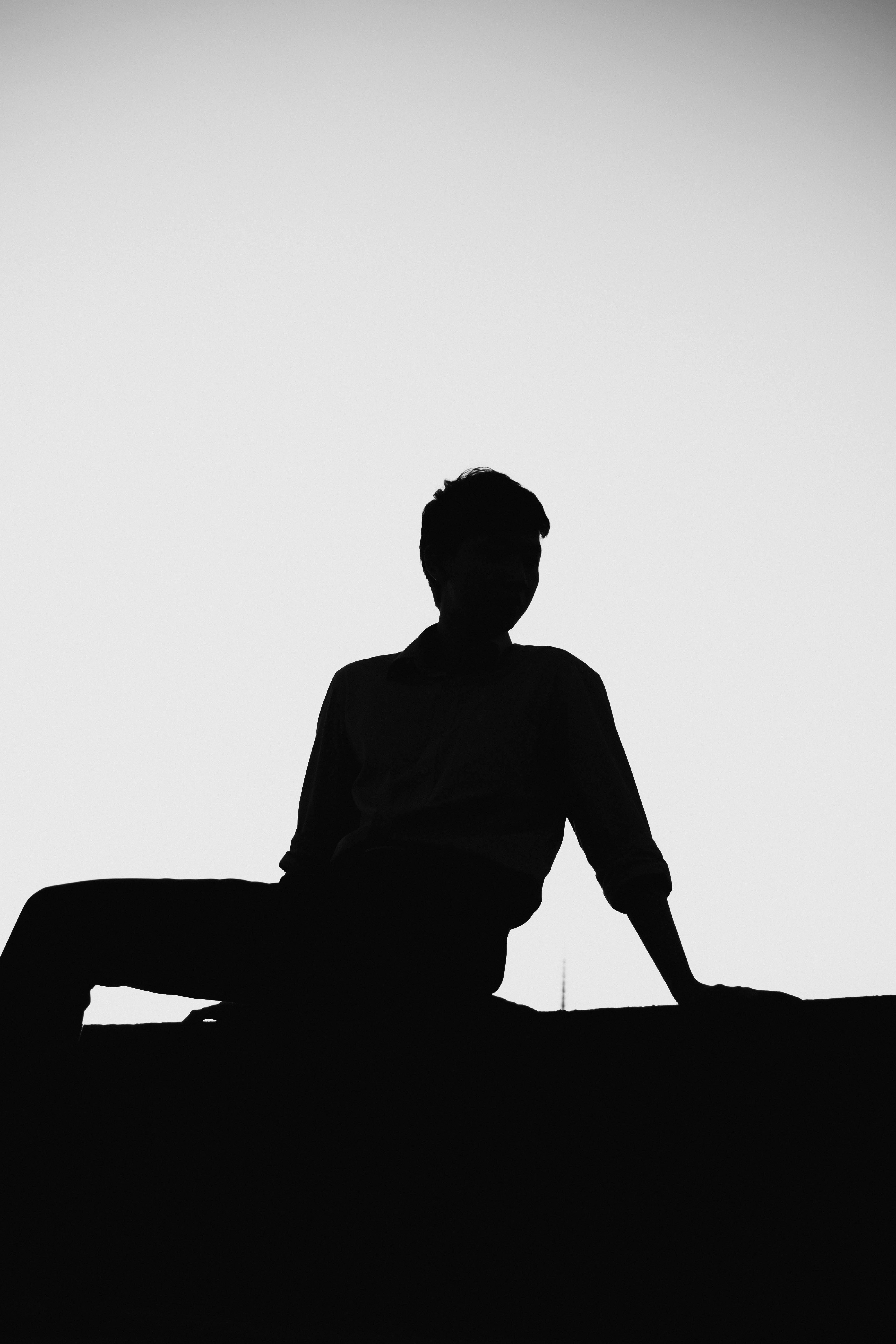 grátis Silhueta artística em preto e branco de uma pessoa descansando contra um céu claro, transmitindo mistério e calma. Foto profissional