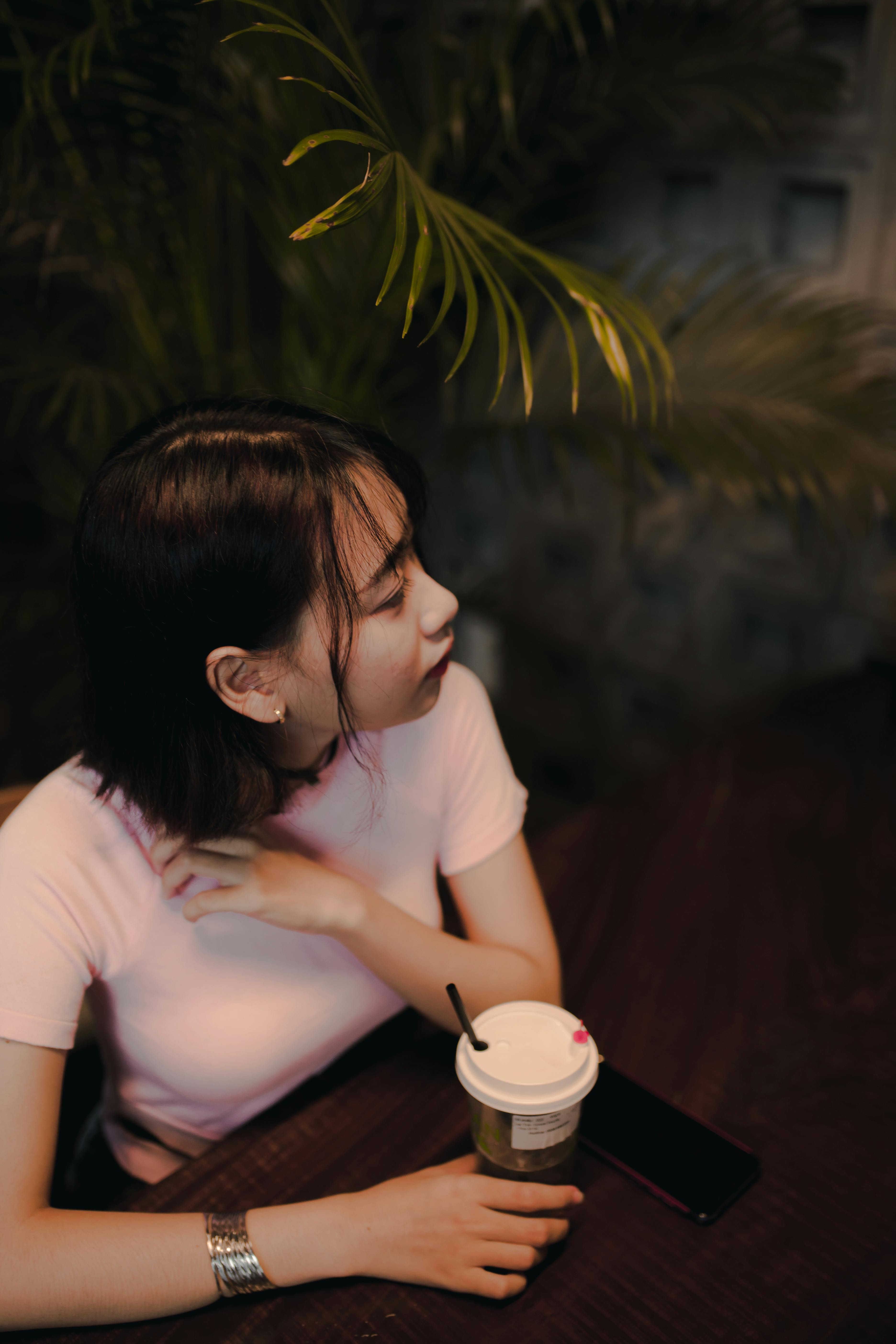 grátis Jovem mulher sentada à mesa de um café, saboreando um café, cercada por plantas de interior. Foto profissional