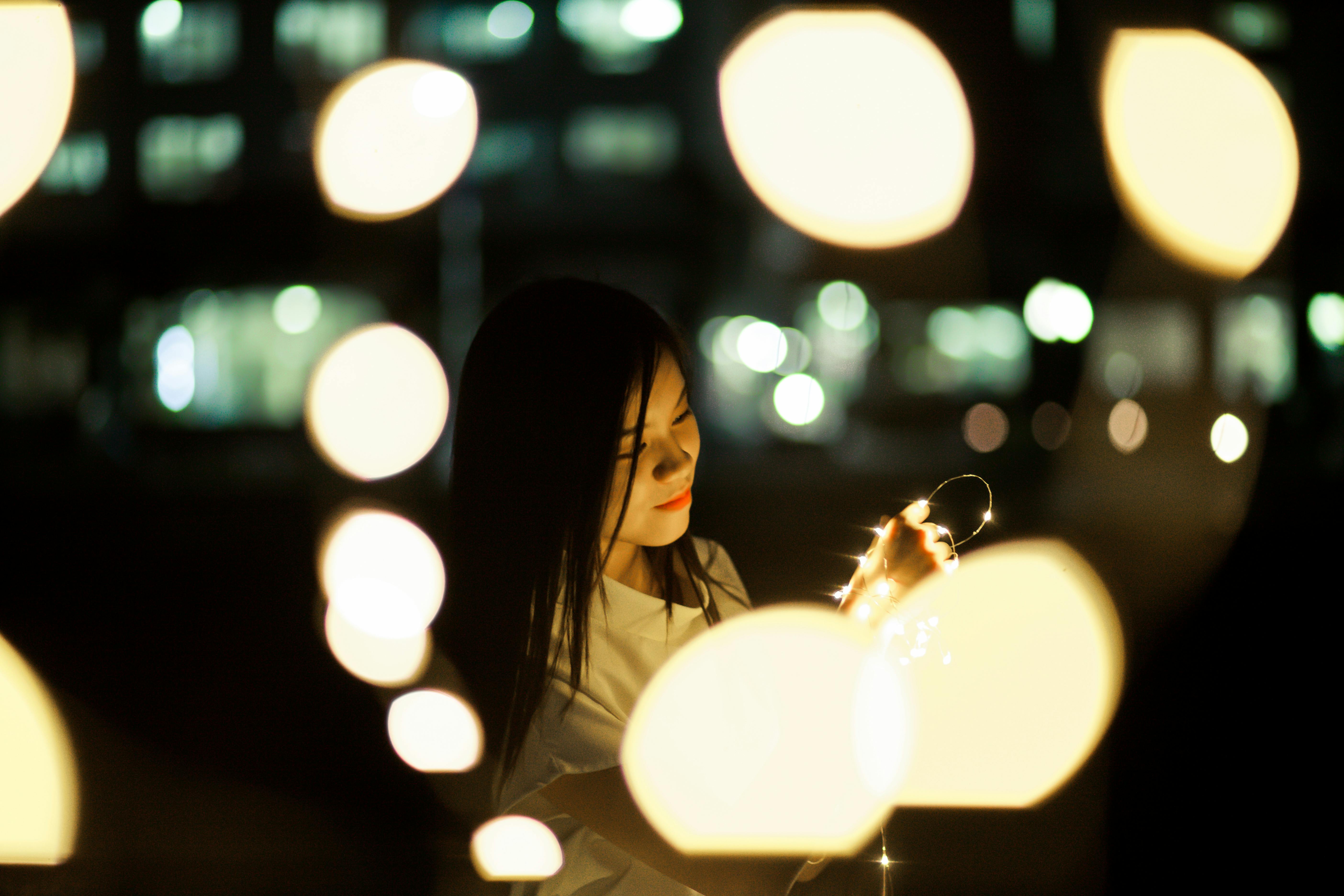 Portrait of a woman holding fairy lights with warm bokeh effect at night.