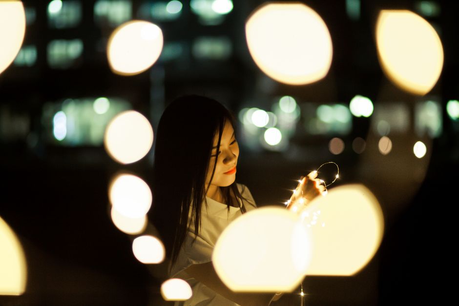 Portrait of a woman holding fairy lights with warm bokeh effect at night.