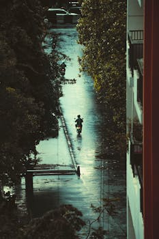 Aerial view of a motorcyclist navigating a rain-soaked street in Jakarta, Indonesia.