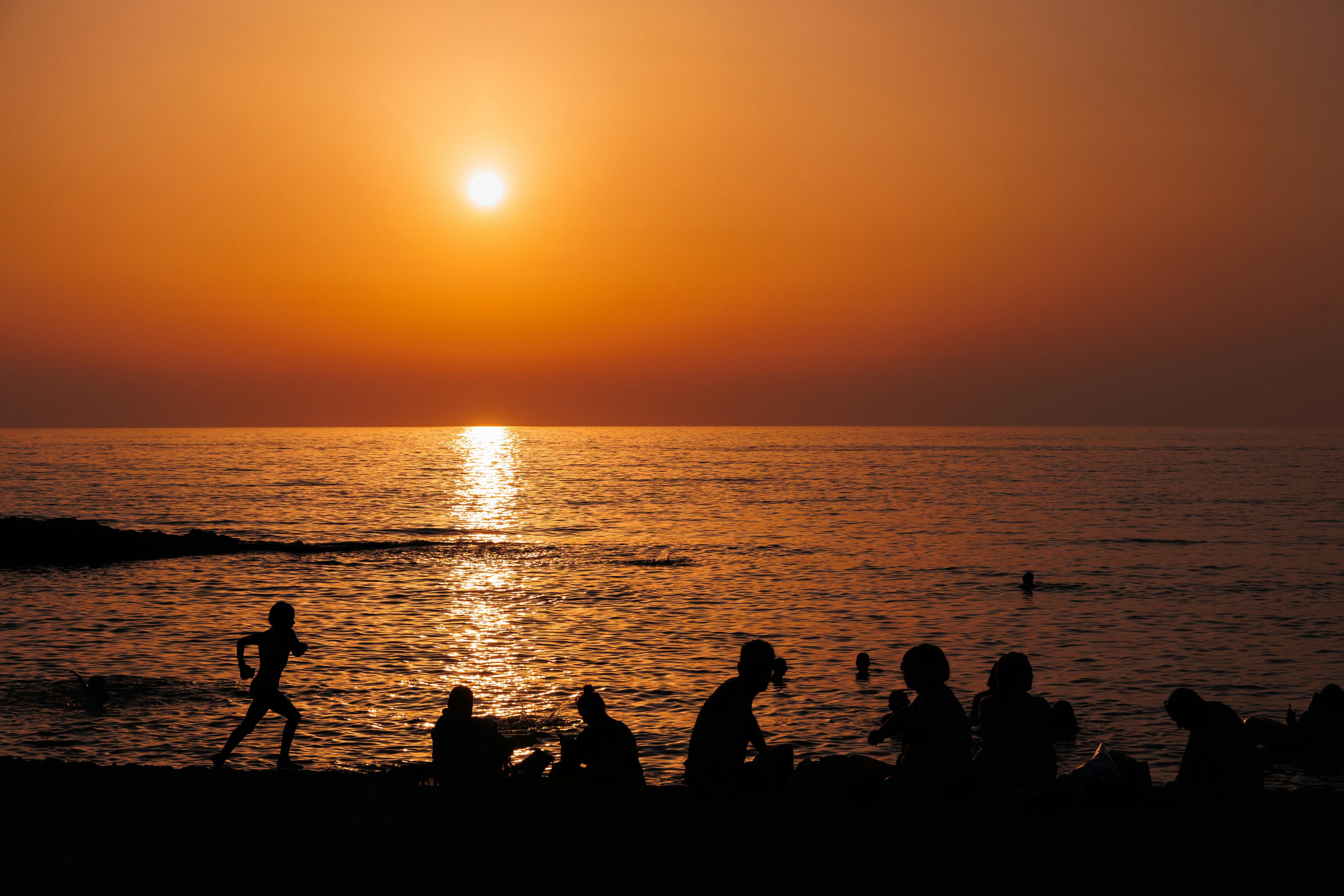 Silhouetted people enjoy a serene beach sunset, capturing nature's beauty.