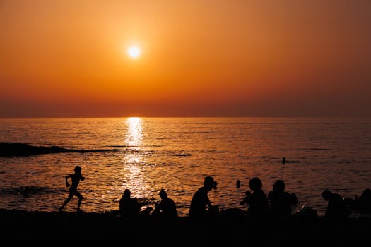 Silhouetted people enjoy a serene beach sunset, capturing nature's beauty.