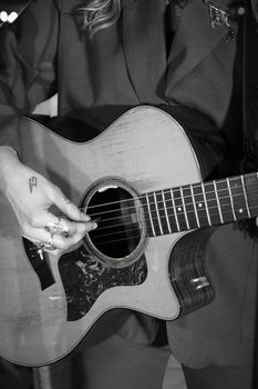 A close-up view of a musician playing an acoustic guitar in a black and white tone.