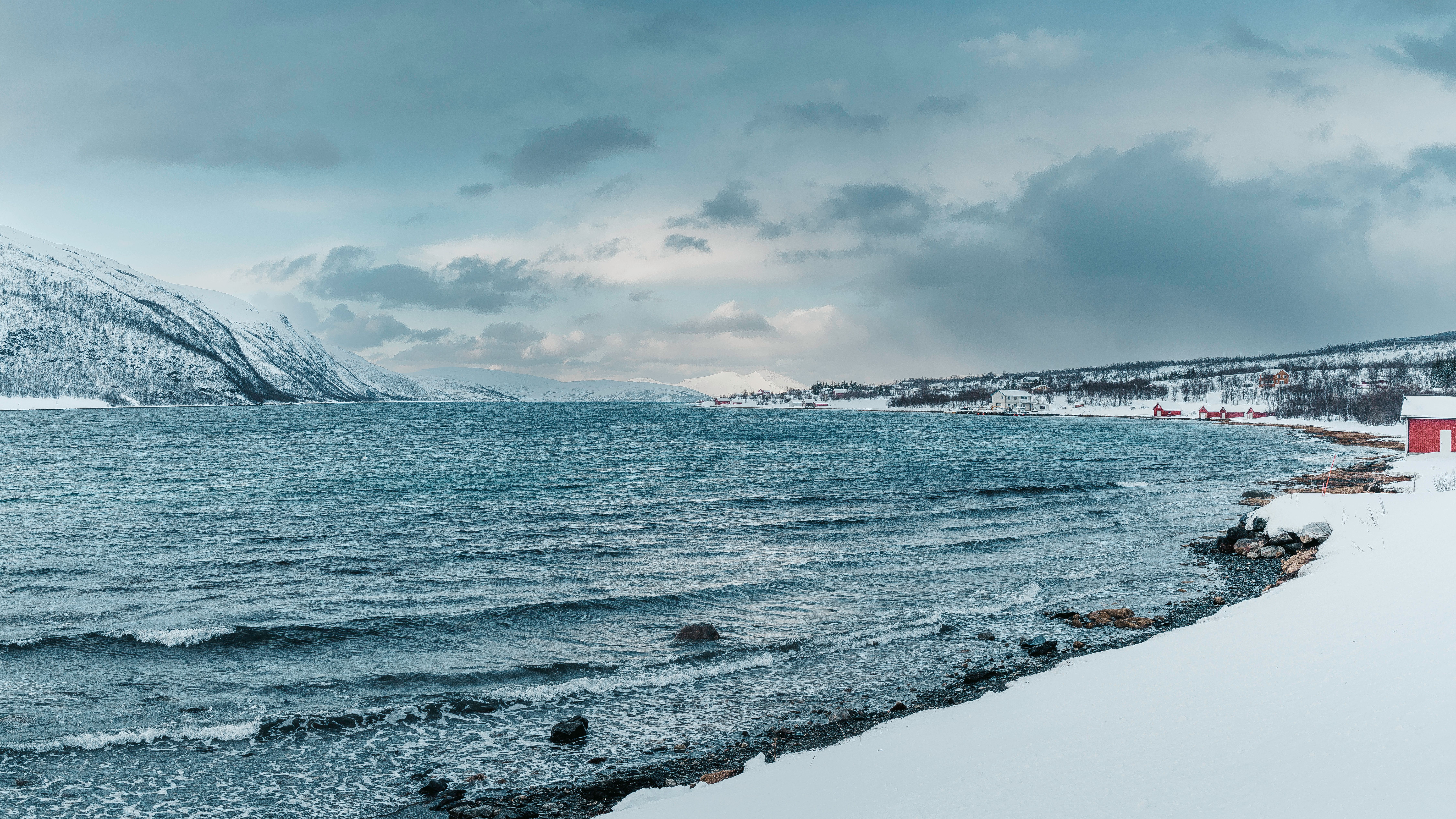 Scenic winter coastline in Norway with snow-dusted mountains fading into an overcast sky
