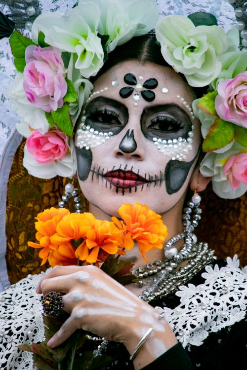 Free A woman with colorful Day of the Dead face paint and floral adornments holding marigolds. Stock Photo