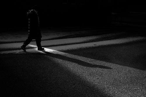 Free A solitary figure walks under dramatic lighting, casting a long shadow on the street. Stock Photo