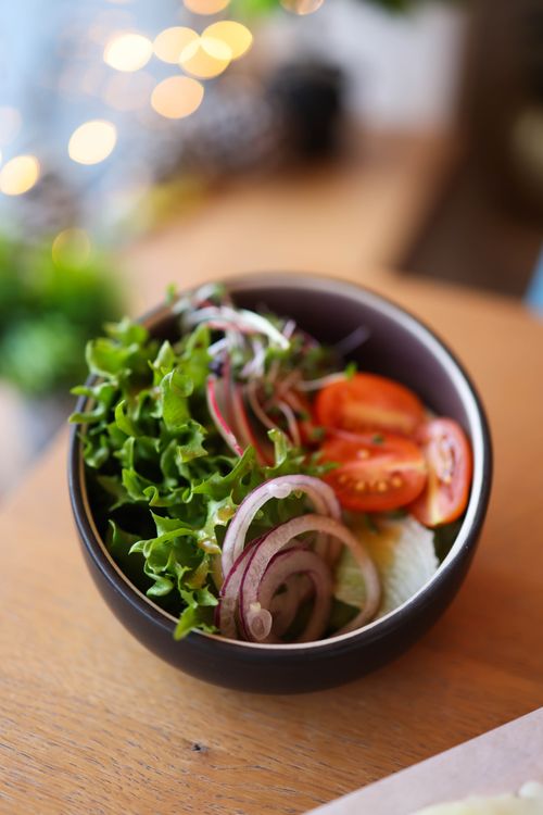 Free Close-up of a fresh salad bowl with lettuce, tomato, and onion slices on a wooden table. Stock Photo