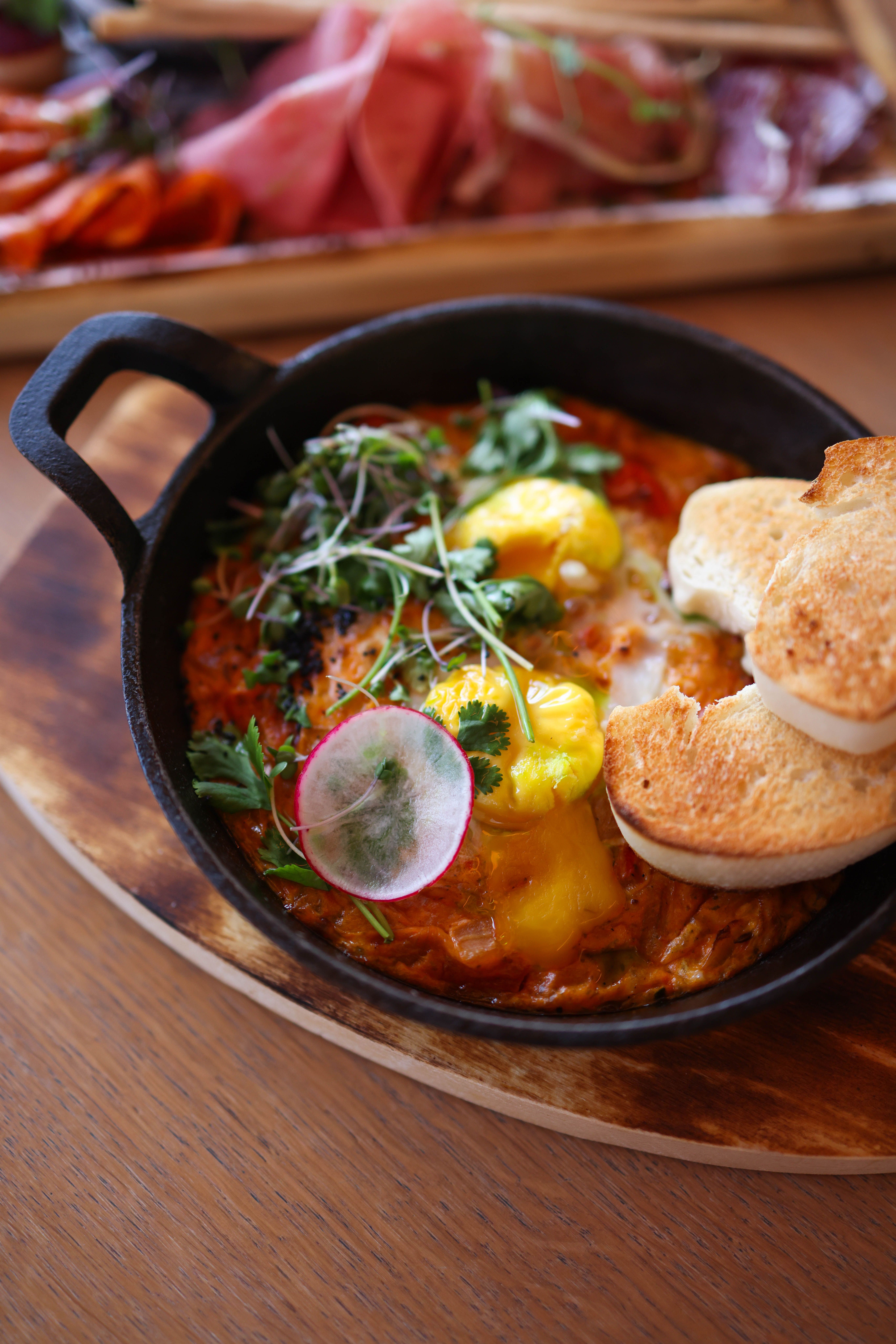 Gratis Gustosa shakshuka in padella con erbe fresche, ravanelli e pane tostato su un tavolo di legno. Foto a disposizione