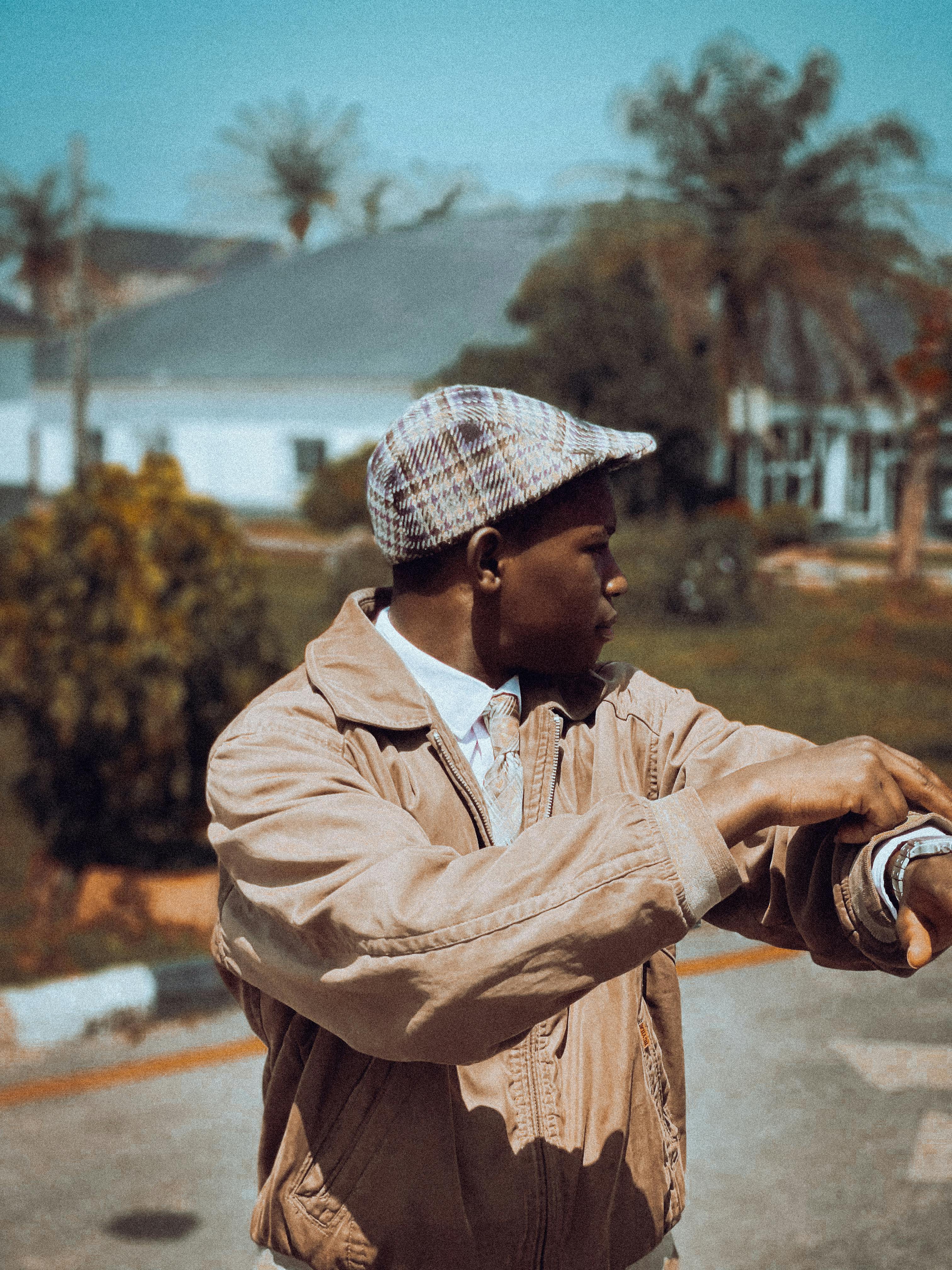 Young man checking his watch outside on a sunny day, wearing a stylish cap and jacket.