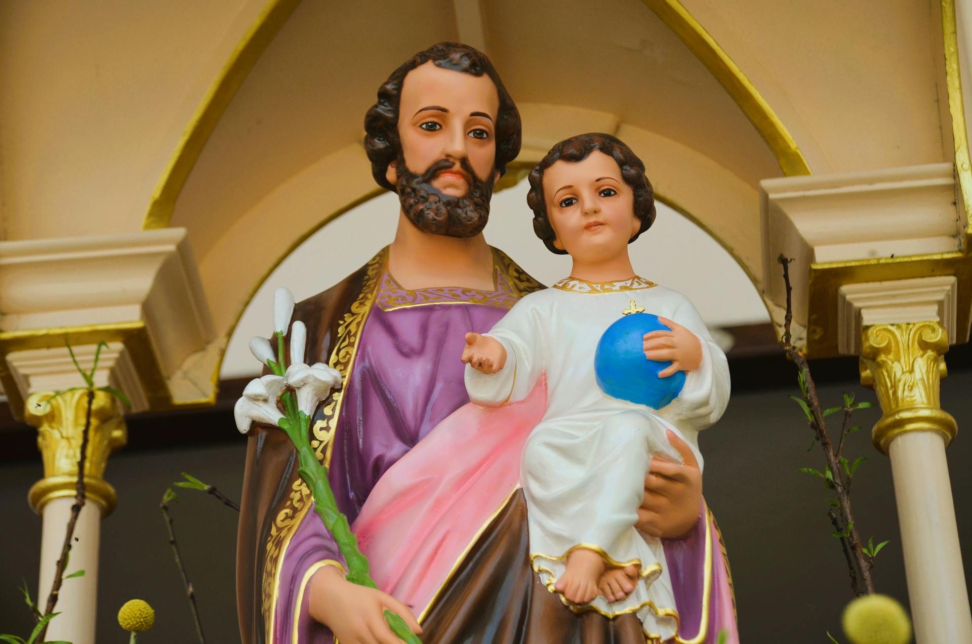 Close-up of a colorful statue of Saint Joseph holding the Child Jesus in a church setting.