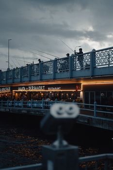 Fishermen line the Galata Bridge at dusk under dramatic clouds in Istanbul, creating a moody cinematic scene.