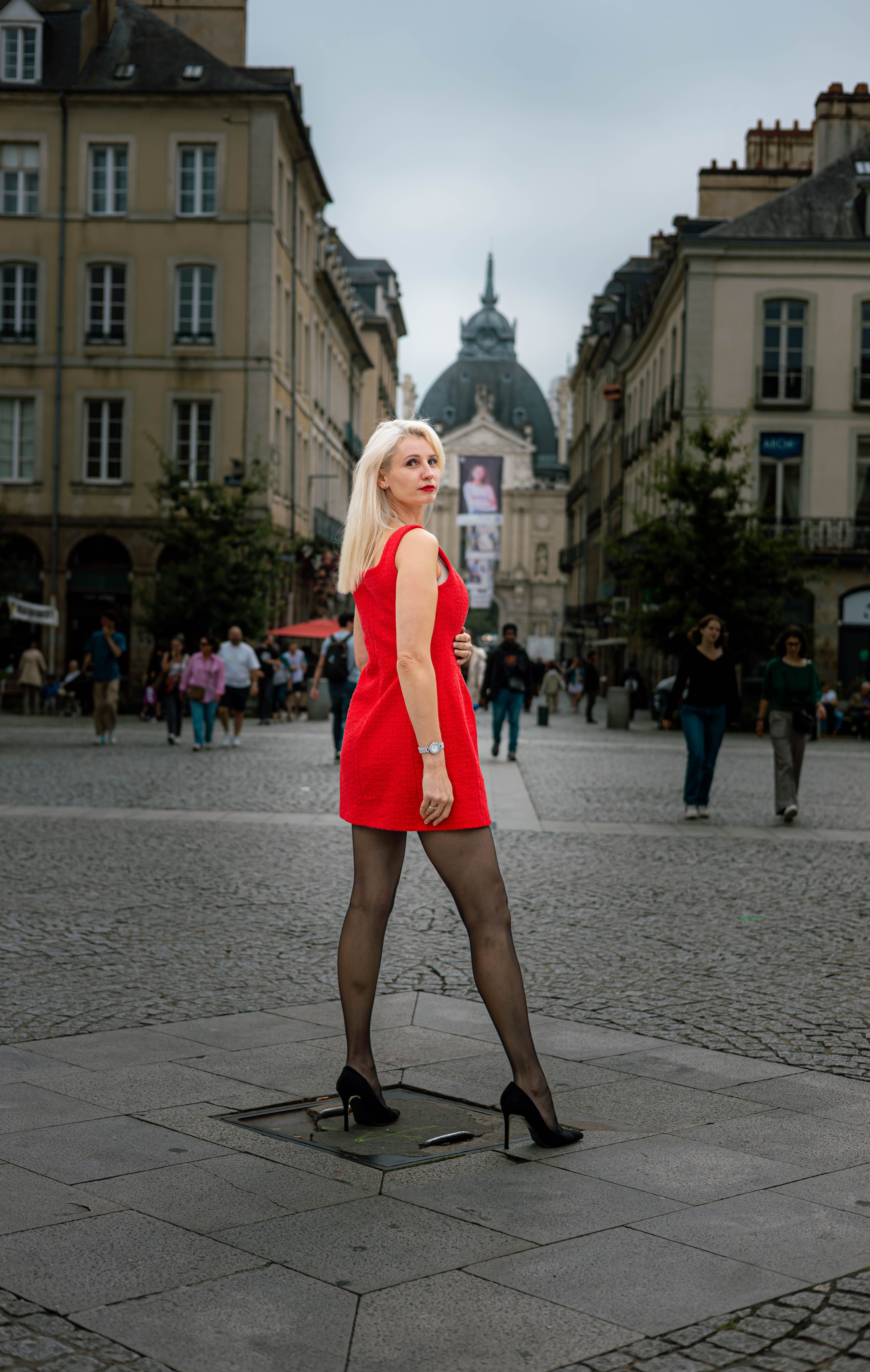 Fashionable woman in a red dress posing confidently in an urban European city square.