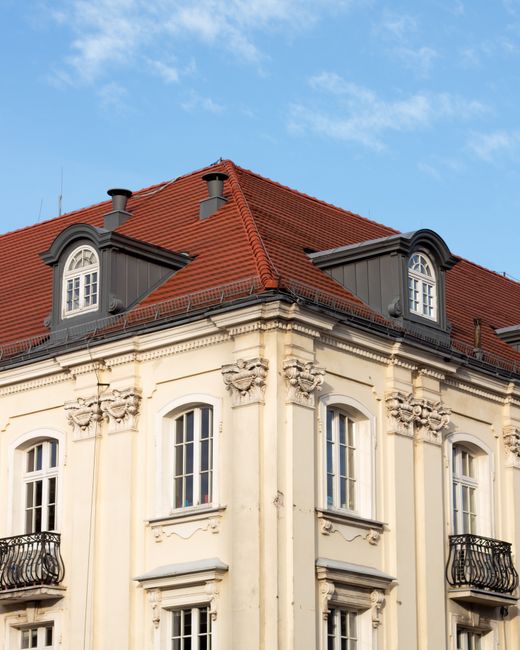 Corner view of a classic European building with red roof and ornate architecture against blue sky.