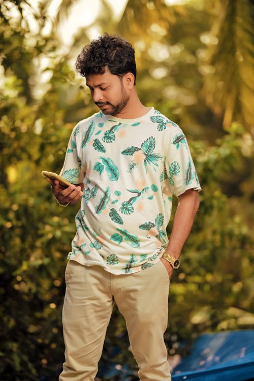 Free Casual young man checks his smartphone while standing in a lush outdoor setting. Stock Photo
