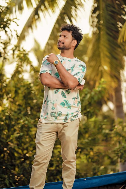 Free A man stands outdoors wearing a tropical print shirt, surrounded by lush palm trees. Stock Photo