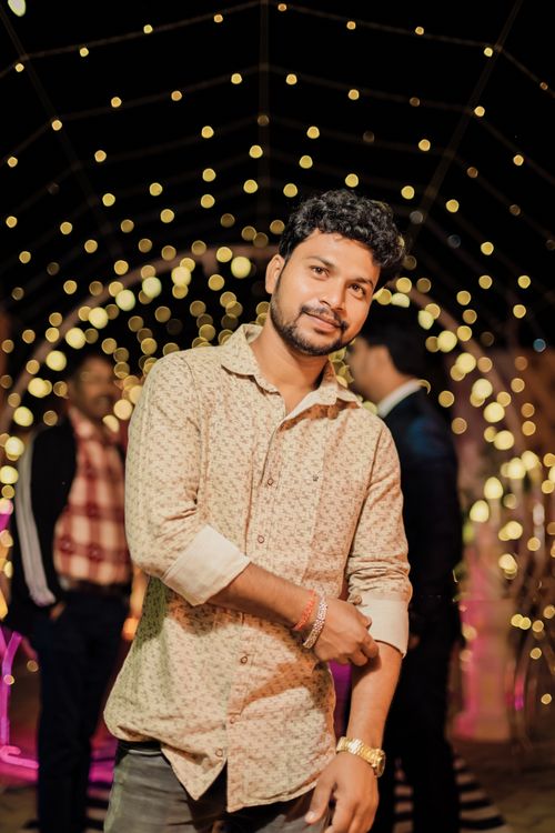 Free A young man stands elegantly at a night event surrounded by festive string lights. Stock Photo