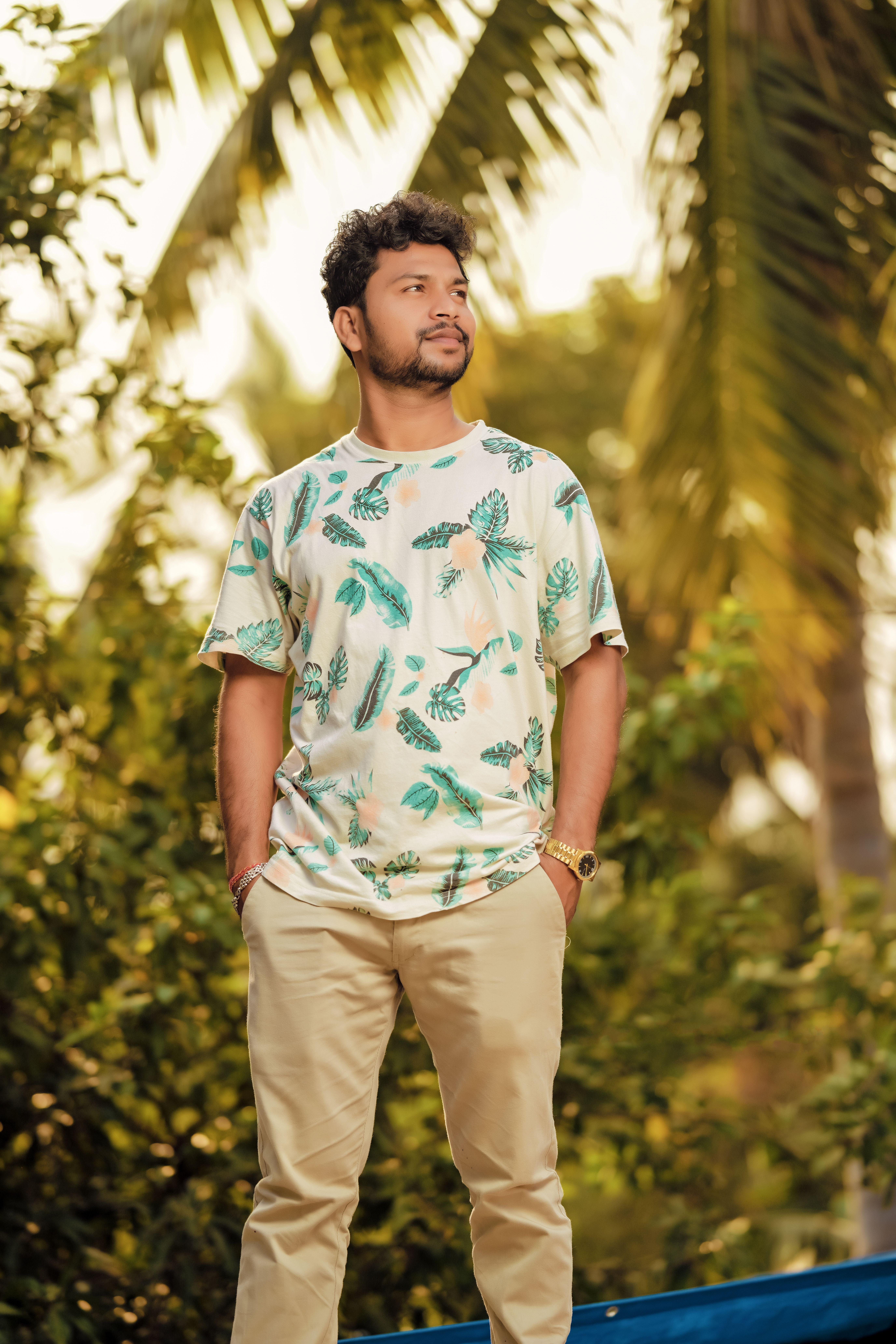 Young man in a tropical floral shirt surrounded by palm trees, exuding a relaxed vibe.