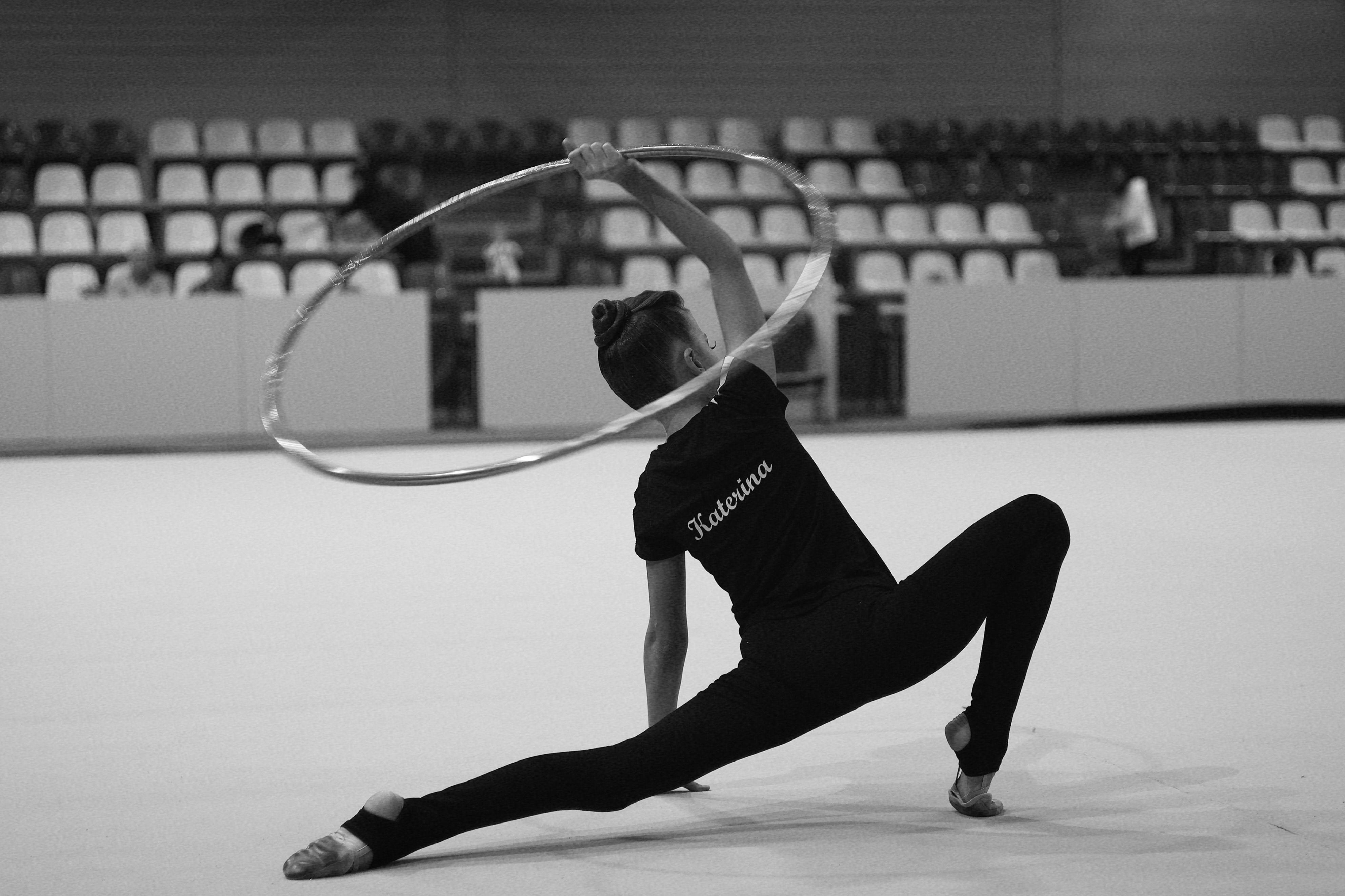 Gymnast in flexible pose with hoop in an indoor arena.