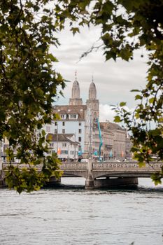 Charming view of Grossmünster framed by trees with a bridge over the Limmat River in Zurich.