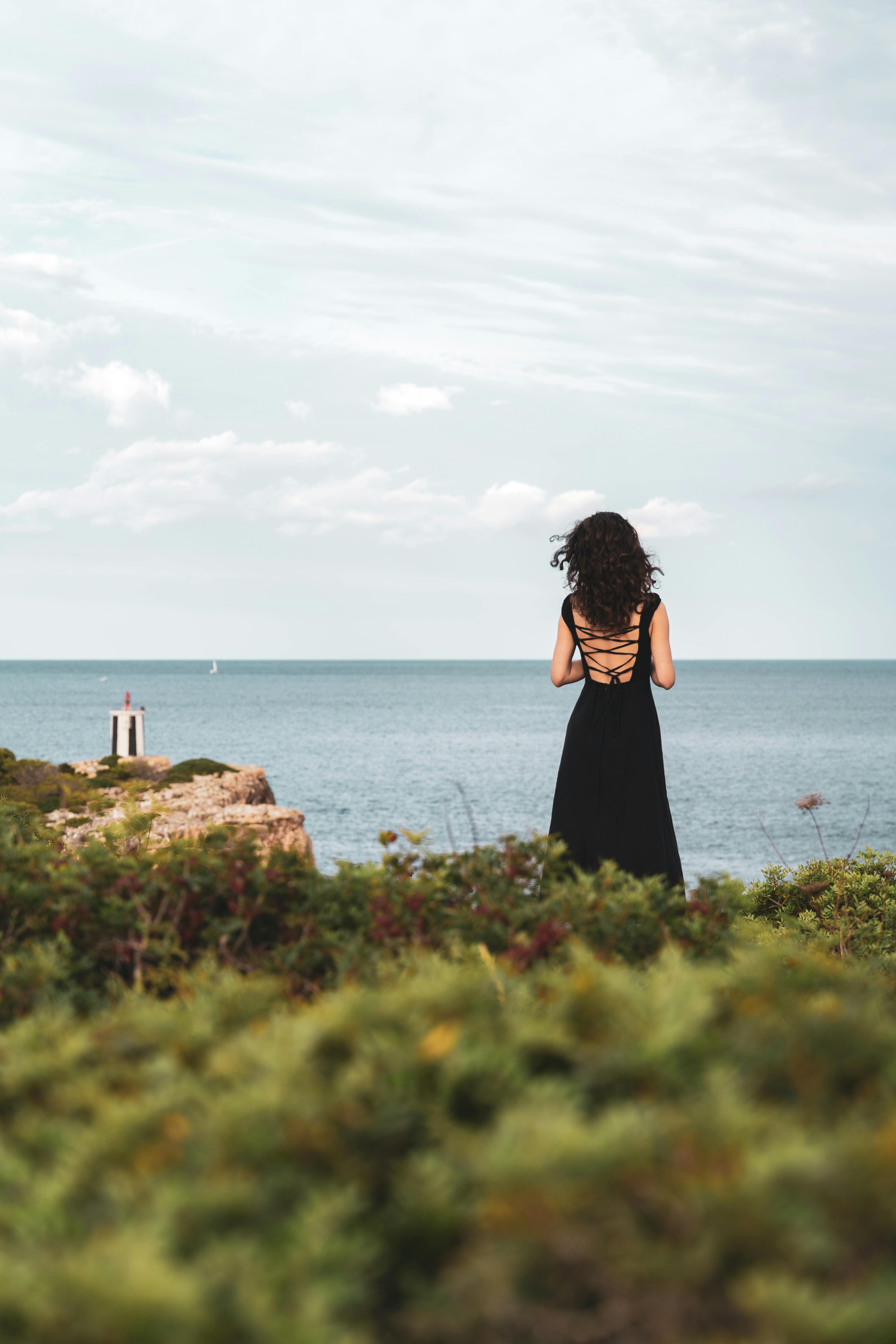 一个穿着黑色连衣裙的女人站在海边，欣赏宁静的海岸景色