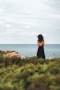 一个穿着黑色连衣裙的女人站在海边，欣赏宁静的海岸景色