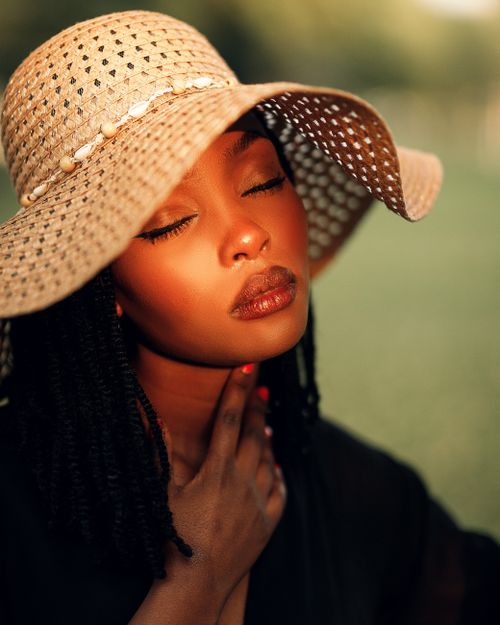 Free Portrait of a stylish woman wearing a sun hat, basking in sunlight outdoors. Stock Photo