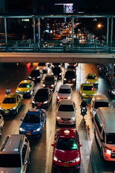 A bustling Bangkok street at night with various taxis and cars.