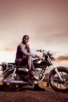 Man in suit sitting on motorcycle during sunset with scenic background.